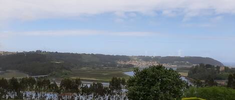 A panoramic view of a coastal town with a river, green hills, and a castle in the distance.