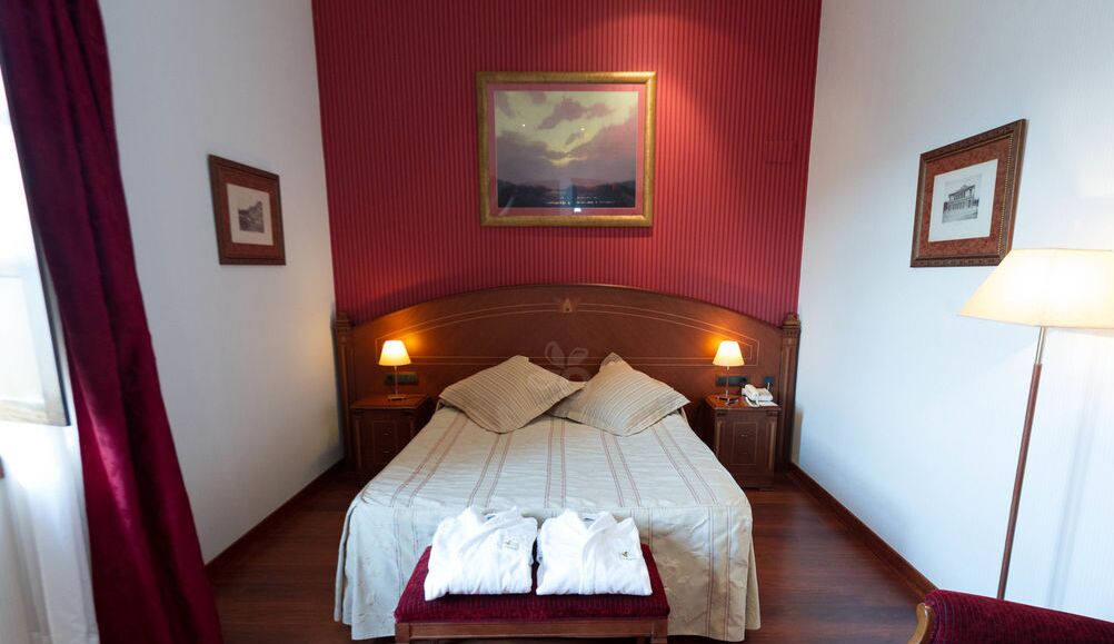 A hotel room with a large bed, two bedside lamps, a headboard, and a framed picture on the wall.