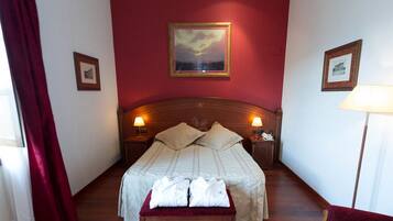 Ein Hotelzimmer mit einem großen Bett, zwei Nachttischlampen, einem Kopfteil und einem gerahmten Bild an der Wand.