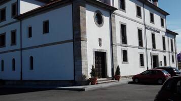 Un edificio bianco con tetto rosso, diverse finestre e un'entrata. Piante in vaso davanti e un'auto rossa parcheggiata nelle vicinanze.