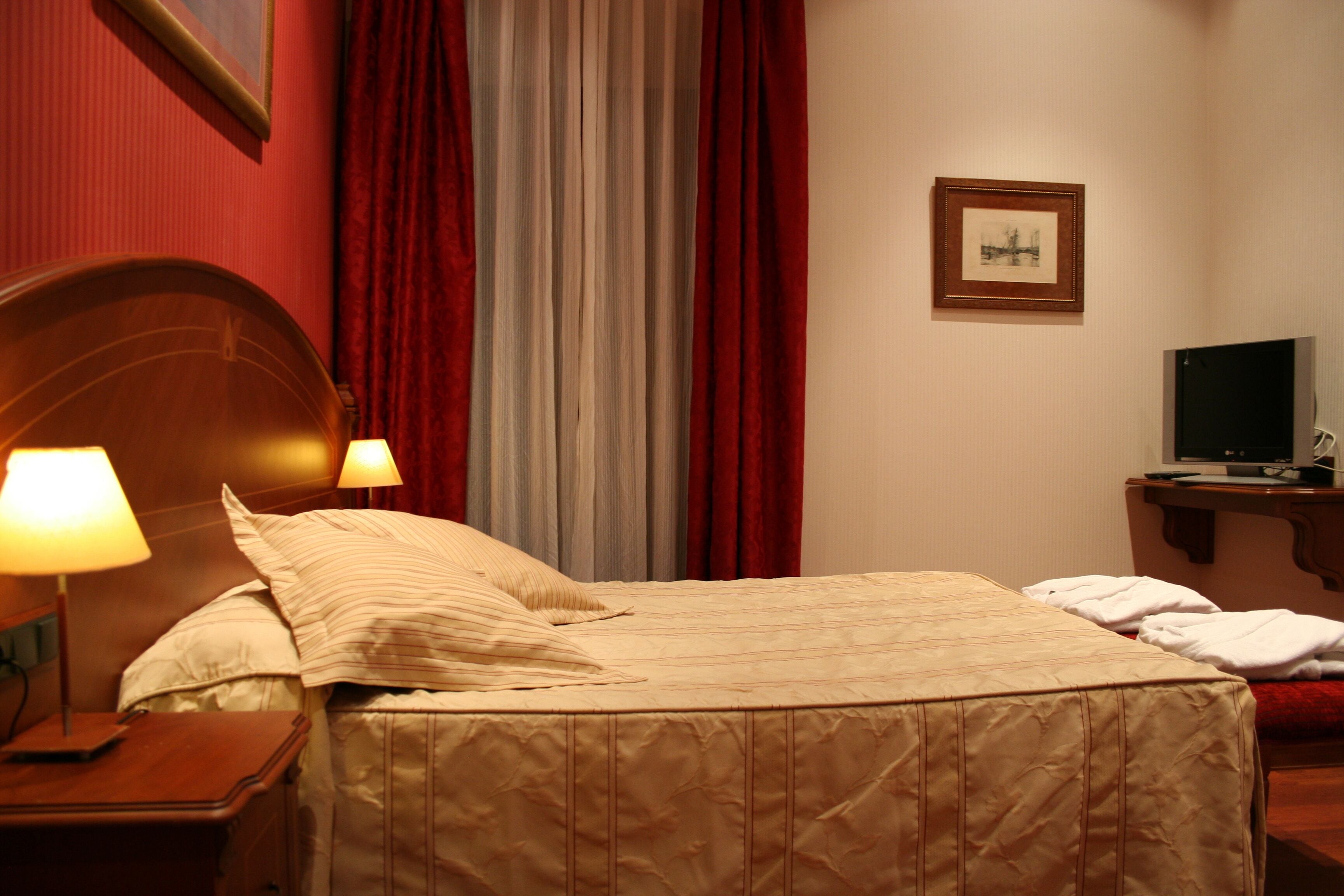 Habitación de hotel con una cama, dos lámparas de noche, un televisor y un cuadro en la pared.