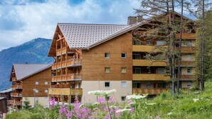 A multi-story wooden building with balconies, surrounded by mountains and wildflowers. - Noemys Les Terrasses de Labrau  (Allos)