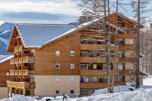 Ein mehrstöckiges Holzhaus mit Balkonen, umgeben von Schnee und Bergen.