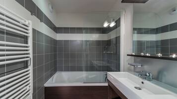 Une salle de bain moderne avec une baignoire, un grand miroir et une cabine de douche en verre.