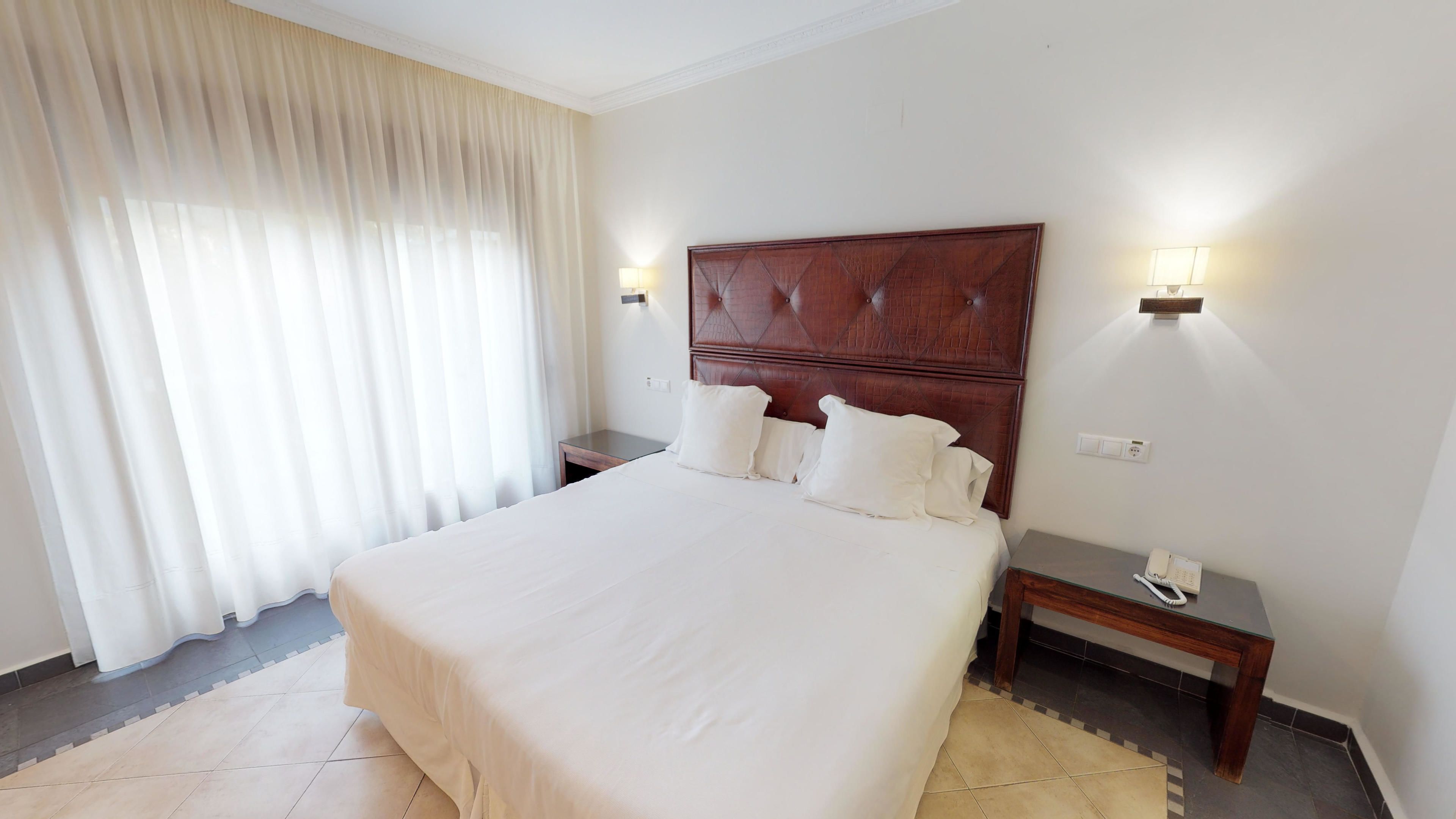 Una habitación de hotel con una cama grande, dos mesitas de noche, una lámpara y un teléfono.