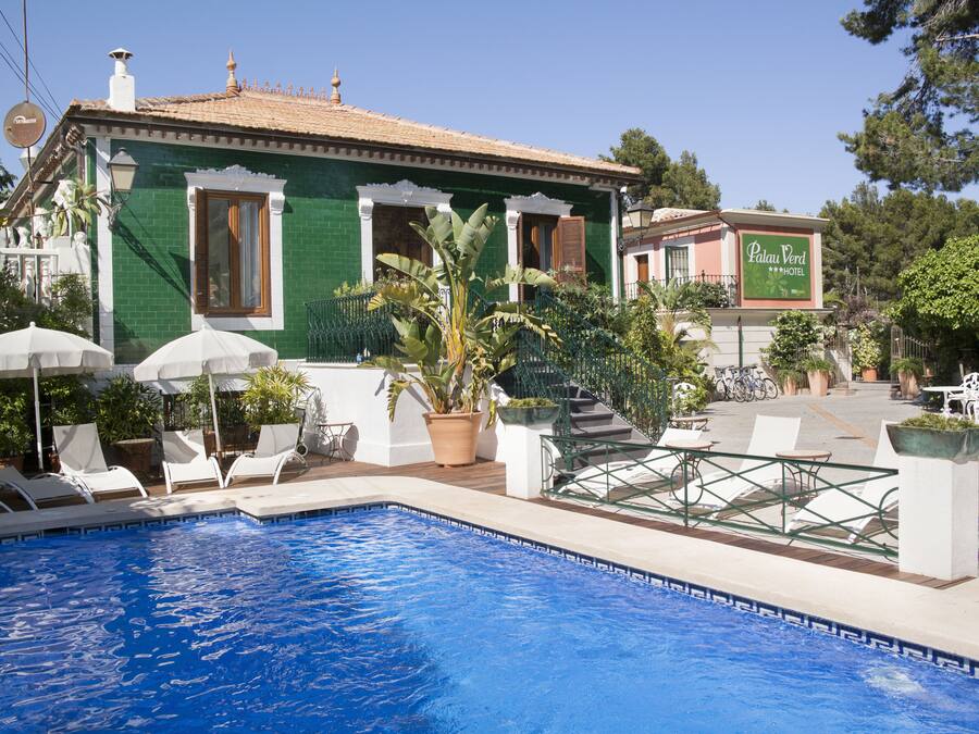 Un hotel con piscina, asientos exteriores y un cartel del Hotel Palau Verde.