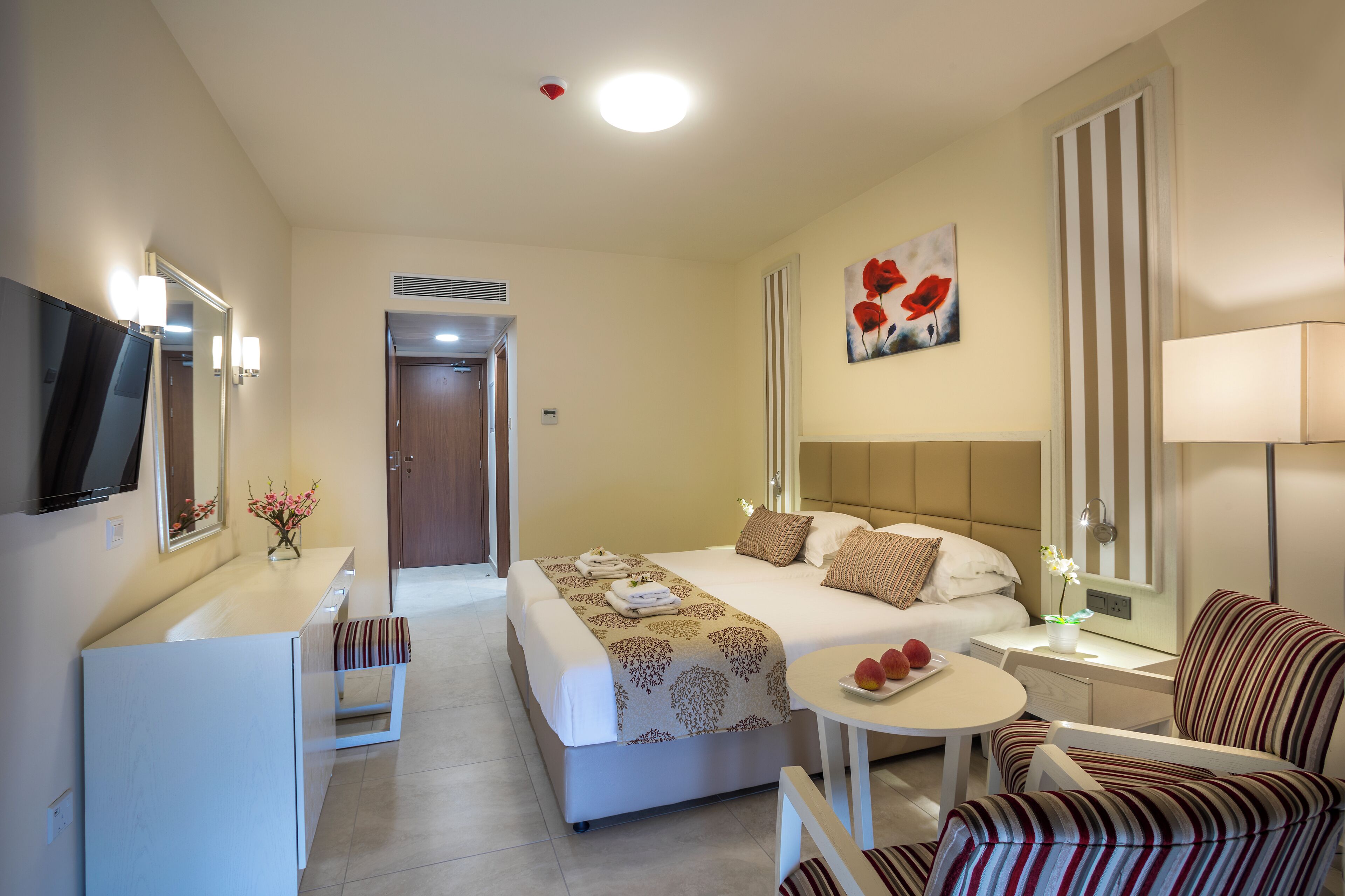 Ein Hotelzimmer mit Bett, Nachttisch, Stuhl, Fernseher und einem kleinen Tisch mit Obst.
