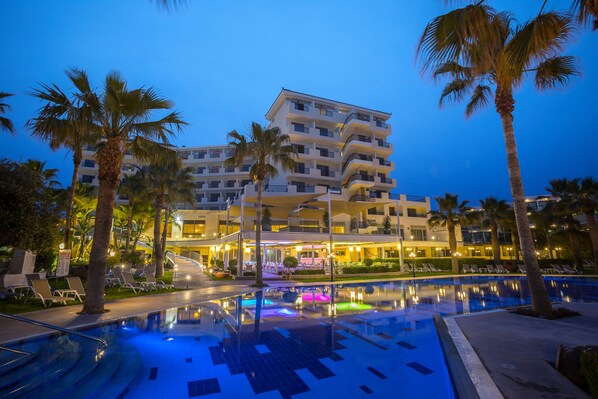 A hotel with a pool, palm trees, and a well-lit entrance.