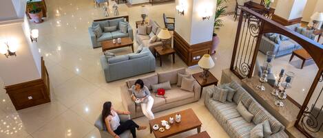 A spacious lobby with multiple seating areas, including sofas and armchairs, arranged around coffee tables and a dining area.