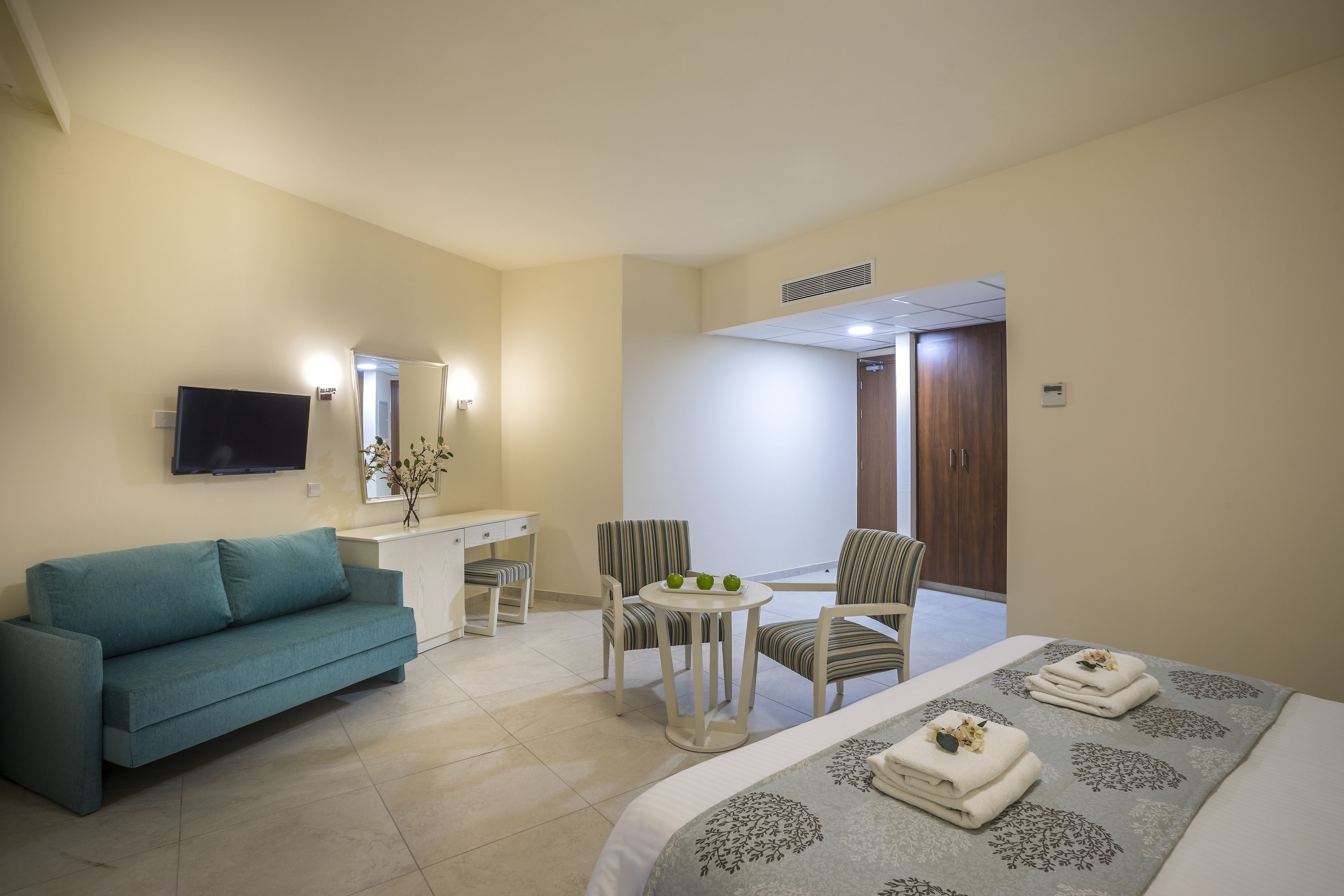 A hotel room with a bed, a sofa, a desk, a chair, and a small table with a vase.