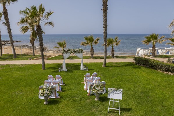 Preparación para una ceremonia de boda con sillas y arreglos florales en un césped con vistas al océano.