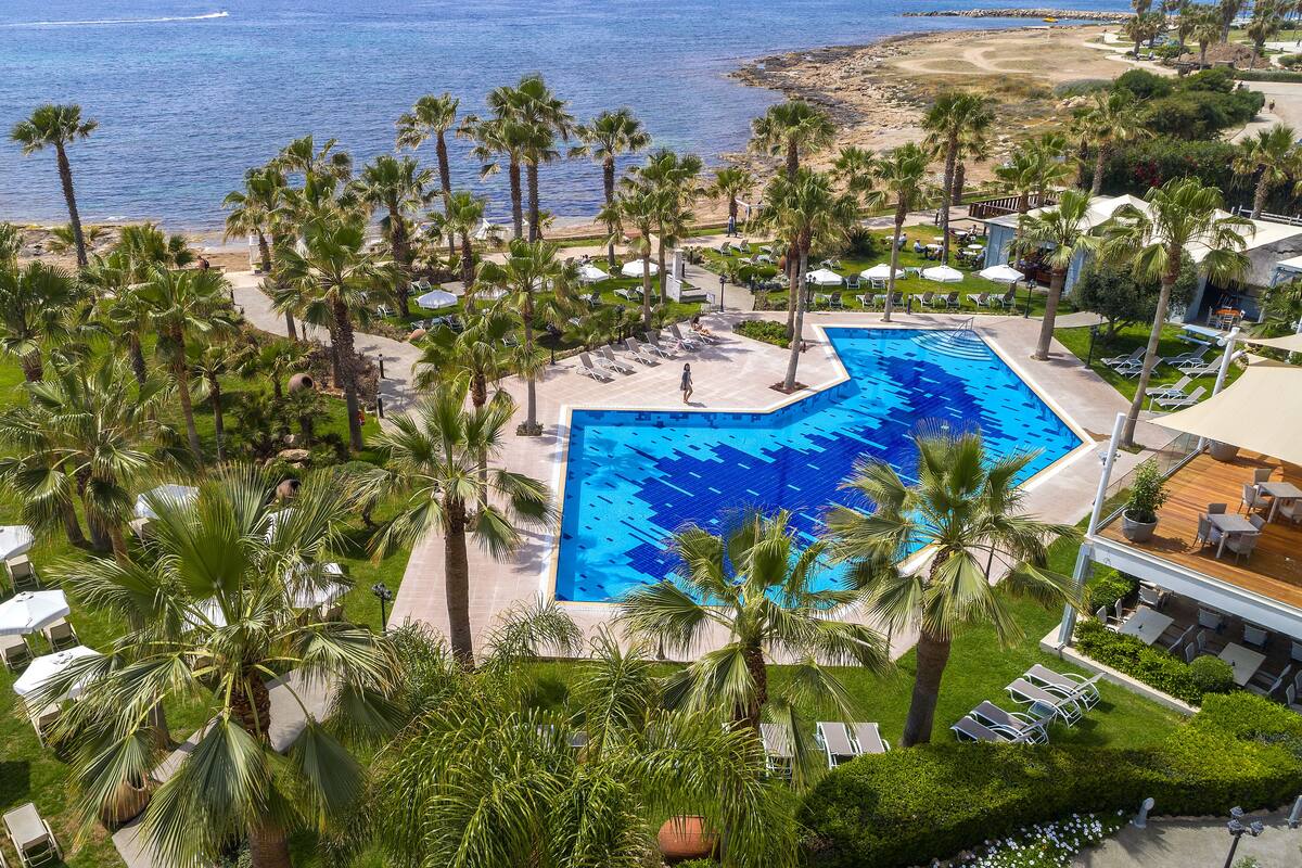 A resort with a large pool, palm trees, and a beach view.