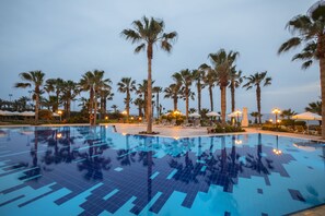 A swimming pool with tiled flooring, surrounded by palm trees and lounge chairs.