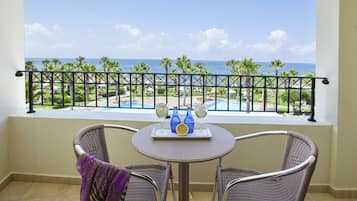 A balcony with wicker chairs, a table with glasses and bottles, and a view of the ocean and pool.