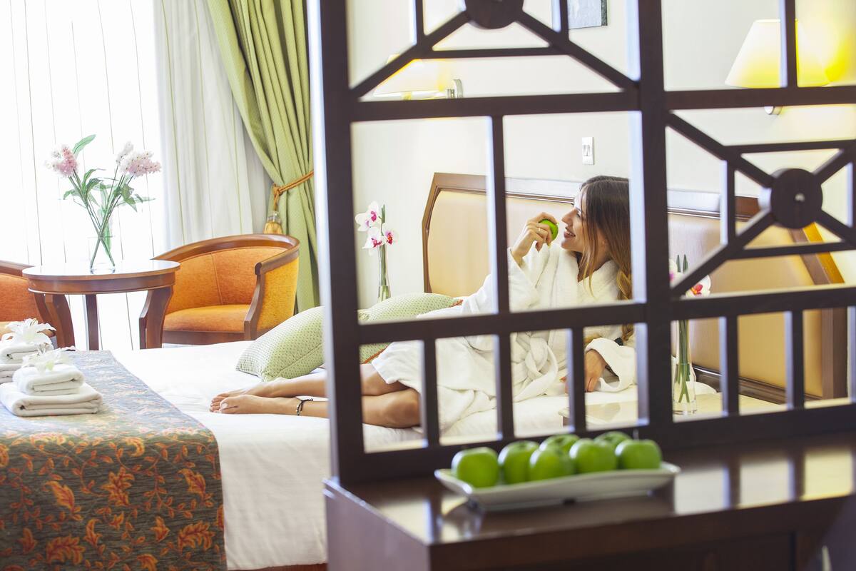 A hotel room with a bed, a bedside table with towels, a chair, and a decorative screen.