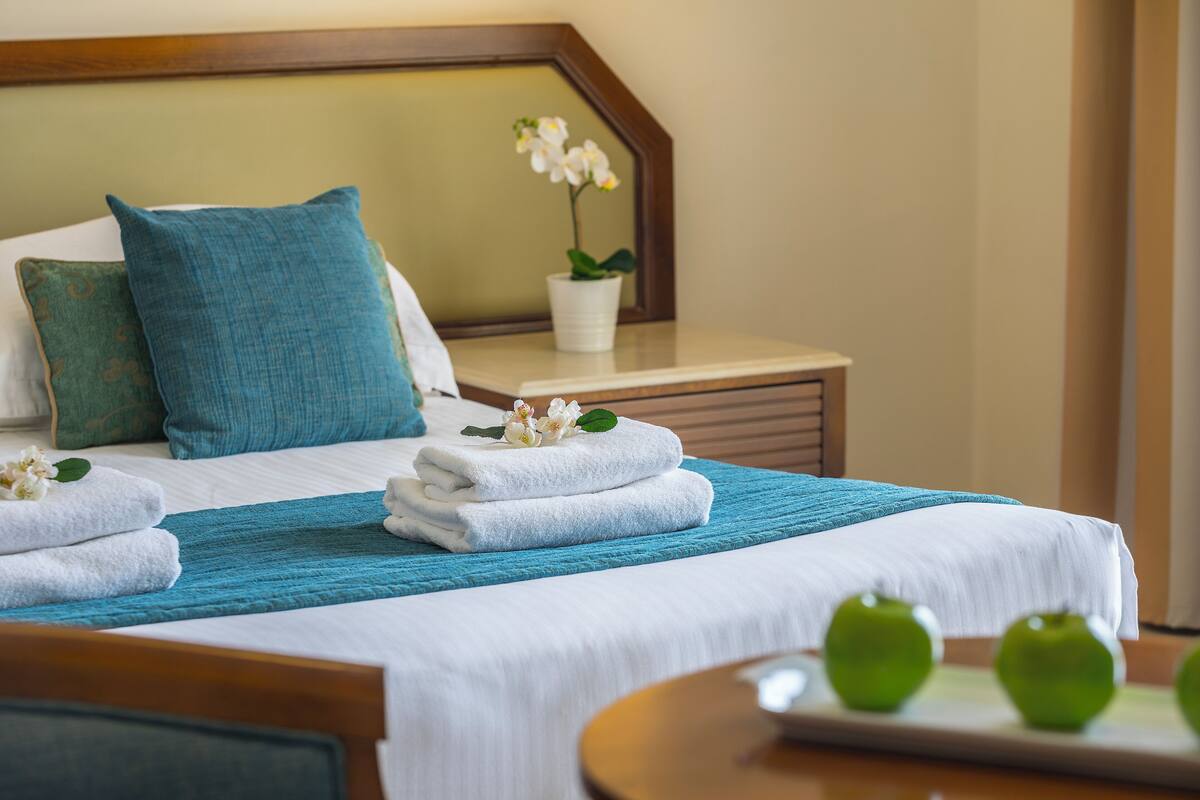 A neatly made bed with white linens, a teal throw blanket, and a small potted orchid on the nightstand.