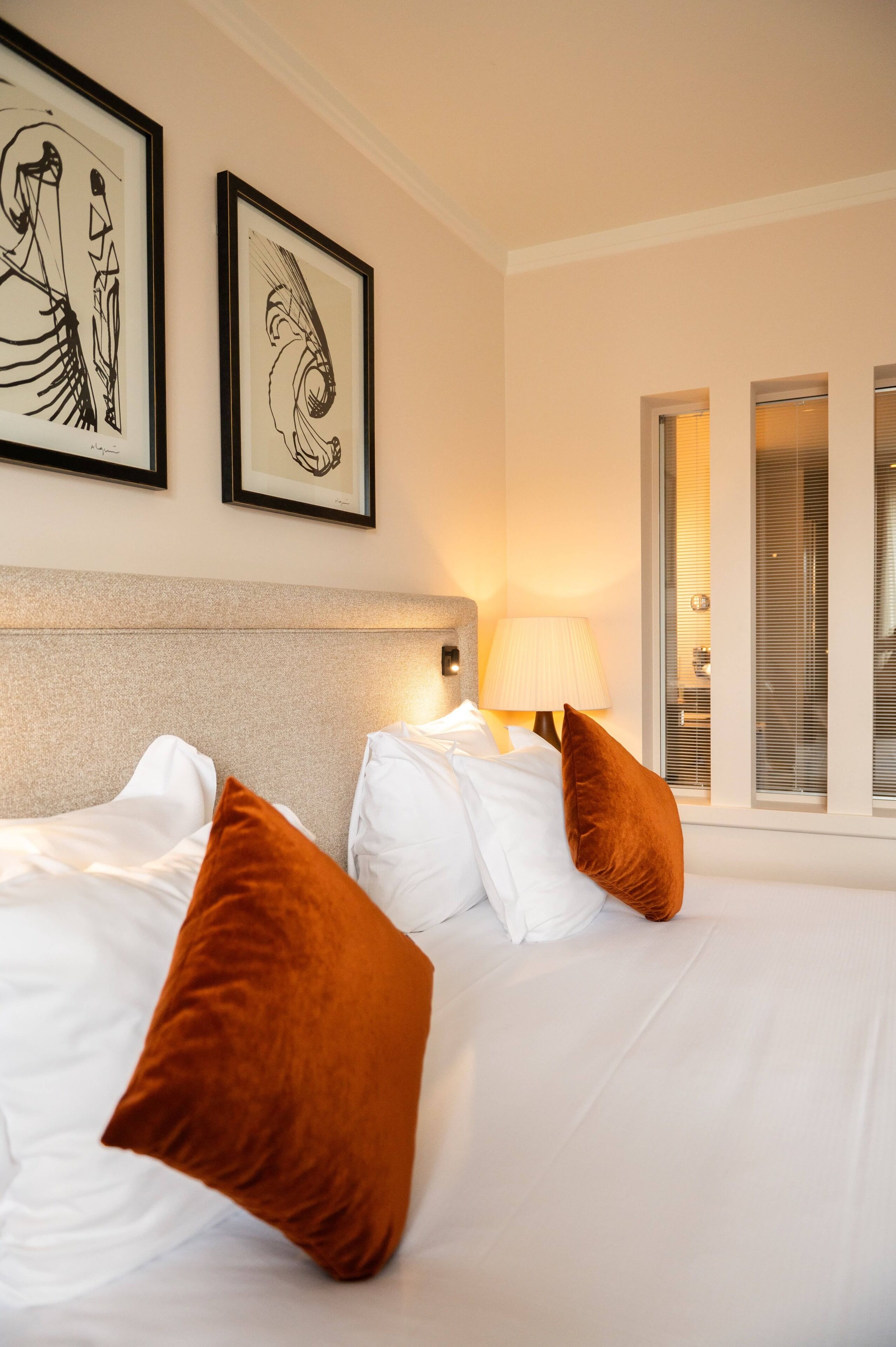 Een hotelkamer met een bed, twee kussens, een lamp en twee foto's in lijsten aan de muur.