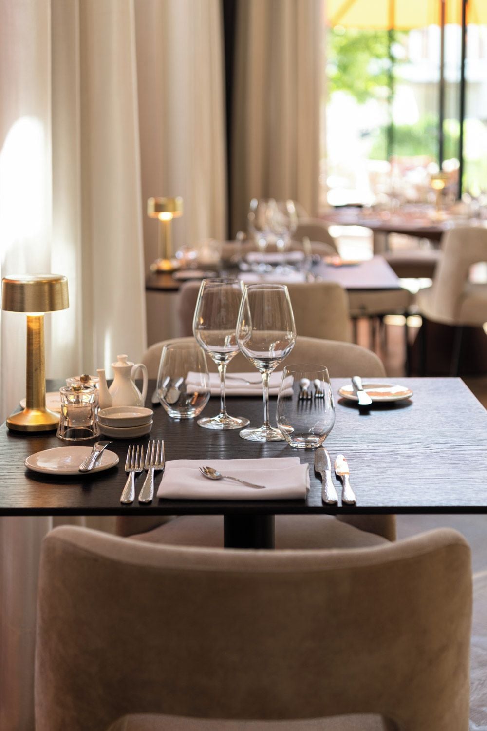 Une table à manger dressée avec des assiettes, des couverts et des verres à vin, avec une lampe et un pichet placés sur le côté.