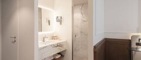 A modern bathroom with a marble vanity, a glass shower enclosure, and a small round table with a chair.