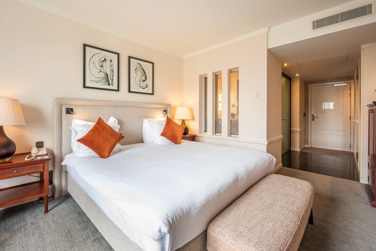 Ein Hotelzimmer mit einem großen Bett, zwei Kissen, einem Nachttisch mit Lampe und gerahmten Bildern an der Wand.