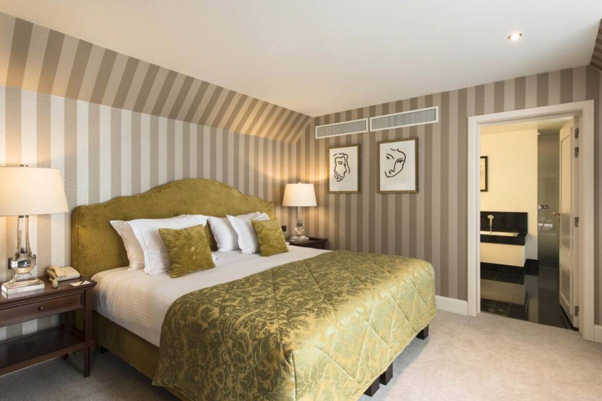Ein Hotelzimmer mit einem großen Bett, gestreifter Tapete, zwei Nachttischlampen und gerahmten Bildern an der Wand.