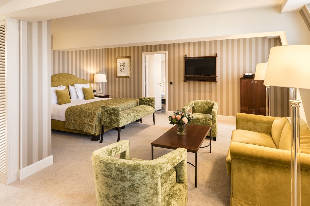 Ein Hotelzimmer mit einem Bett, zwei Sessel, einem Sofa, einem Couchtisch, einem Fernseher und einer Lampe.