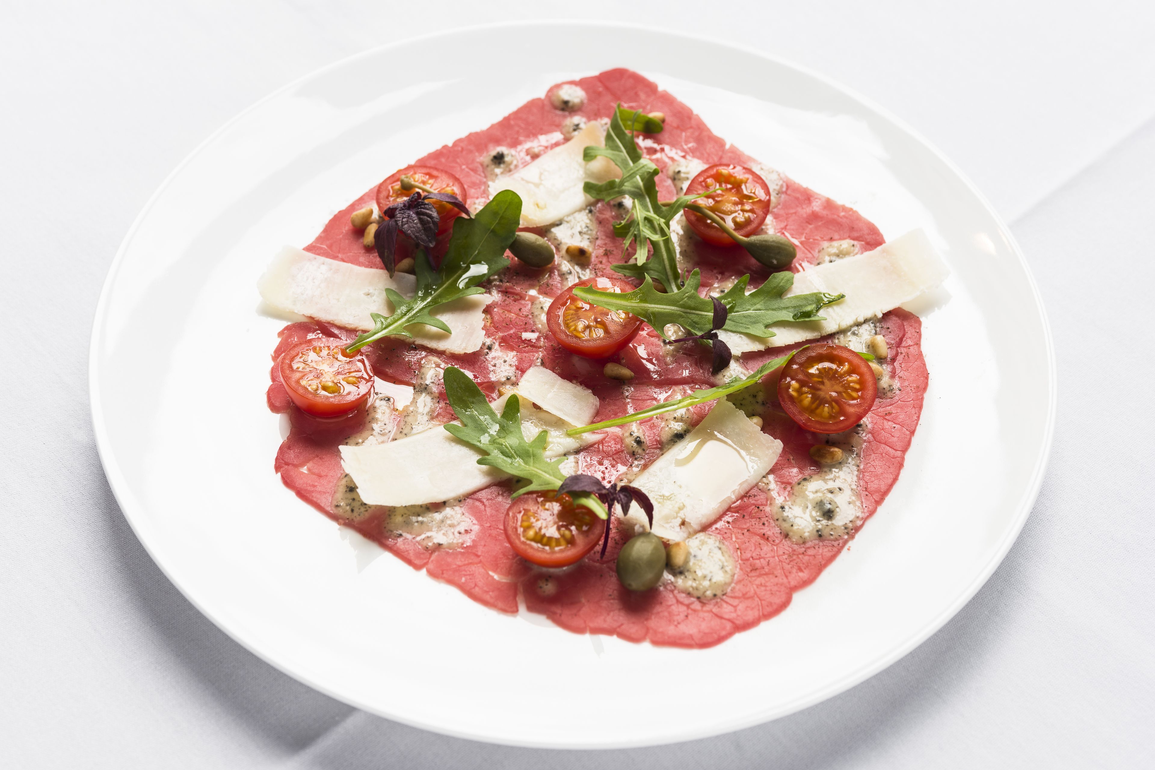 A plate of food with thinly sliced meat, cheese, and cherry tomatoes.