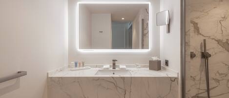 Un baño moderno con lavamanos de mármol, un espejo grande con iluminación integrada y una ducha con mampara de vidrio.