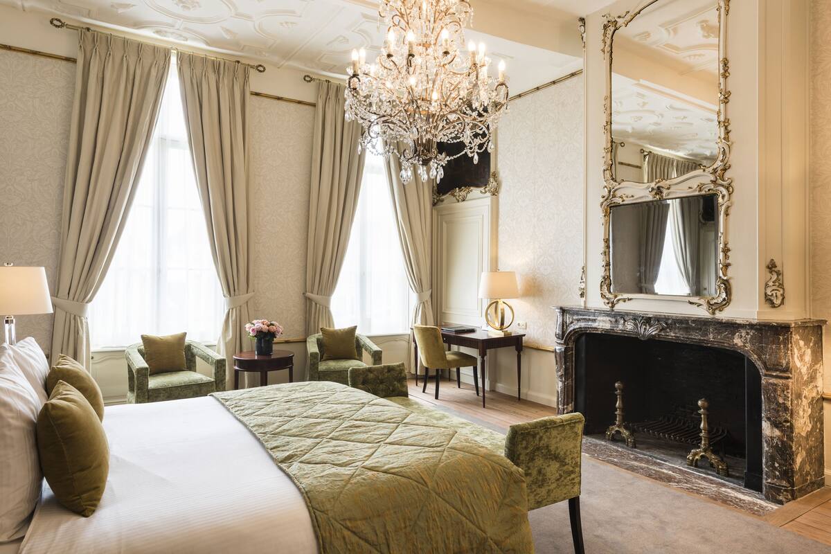 Ein Hotelzimmer mit einem großen Bett, einem Kamin, einer Kristallleuchter und einem Spiegel.