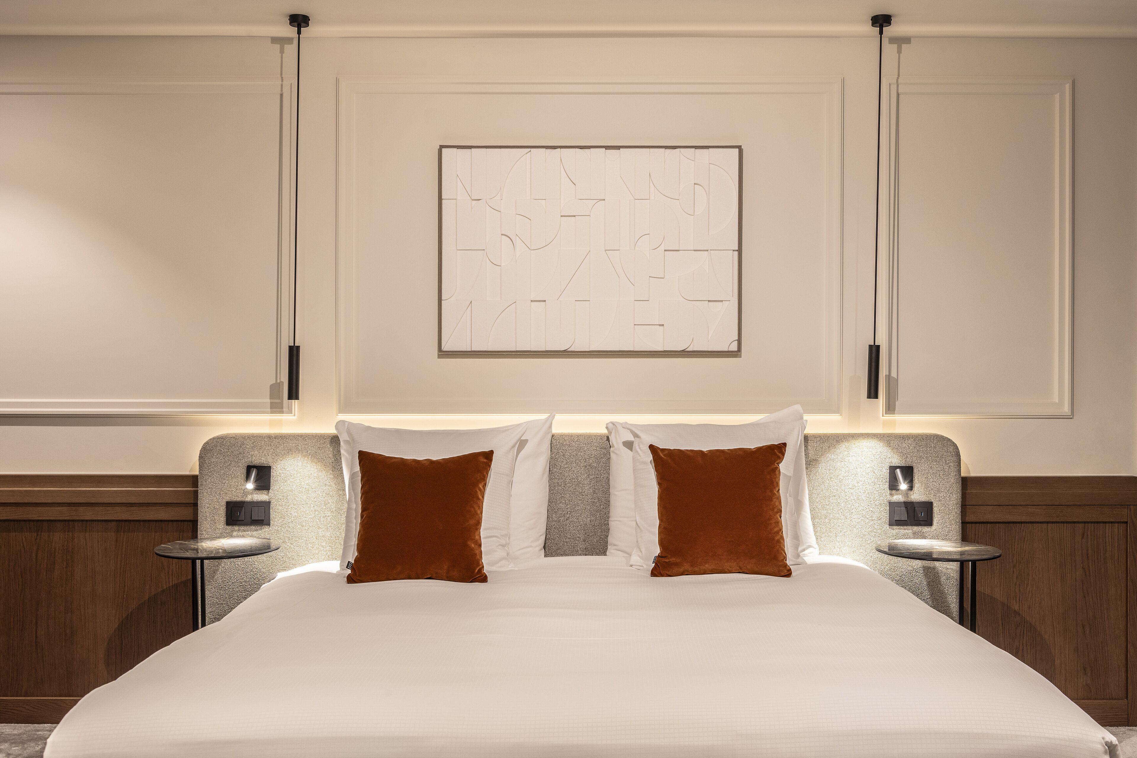 Quarto de hotel com uma cama grande, duas mesas de cabeceira, uma obra de arte pendurada na parede e uma cabeceira de madeira.