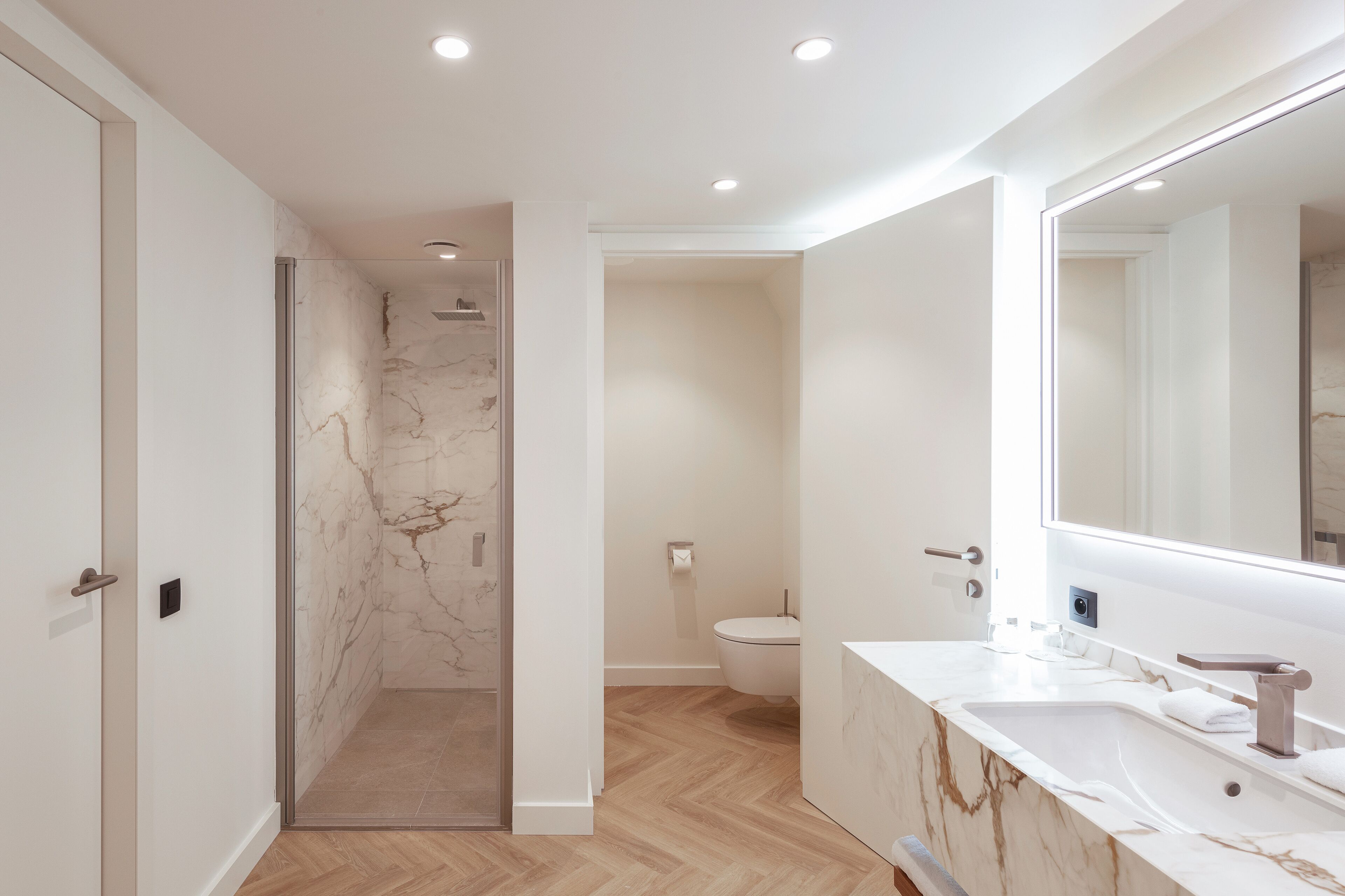 A modern bathroom with a marble vanity, a glass-enclosed shower, and a toilet.
