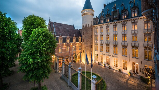 A historic building with a prominent tower, a courtyard with a fountain, and a well-lit facade. - Dukes’ Palace – by Dukes’ Hotel Collection (Bruges)