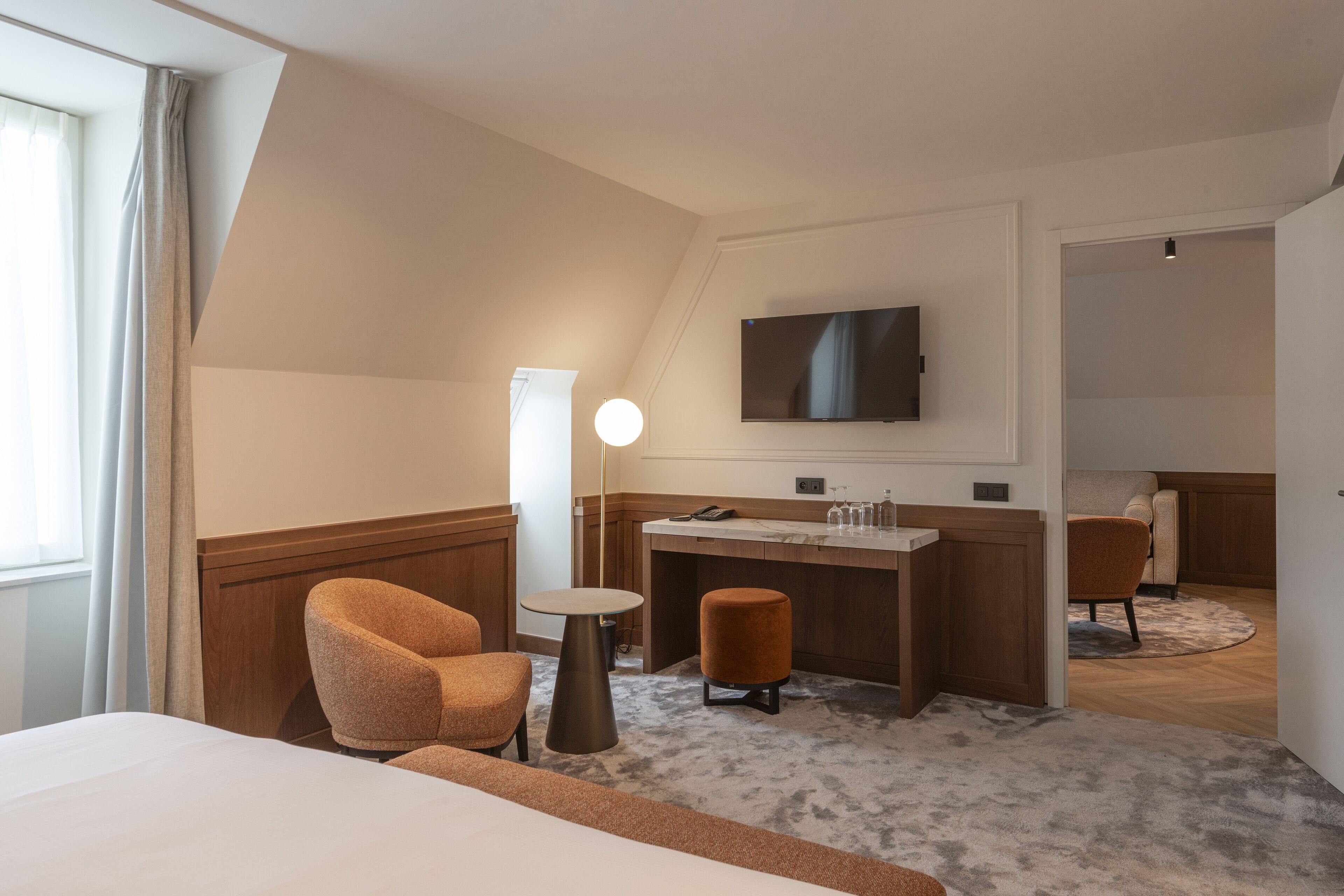 A hotel room with a bed, a desk, a chair, a television, and a large window.
