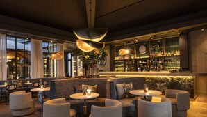 A bar area with round tables, cushioned seating, a large plant, and a wine display. - Dukes’ Palace – by Dukes’ Hotel Collection (Bruges)