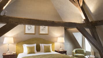 Un dormitorio con techo alto, vigas de madera a la vista, una cama grande con ropa de cama verde, dos mesitas de noche con lámparas y cuadros en la pared.