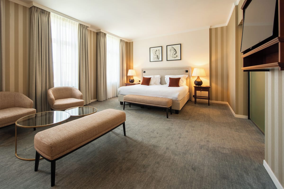 Ein Hotelzimmer mit einem Bett, zwei Nachttischen, einem Sofa, einer Bank und einem Glastisch.