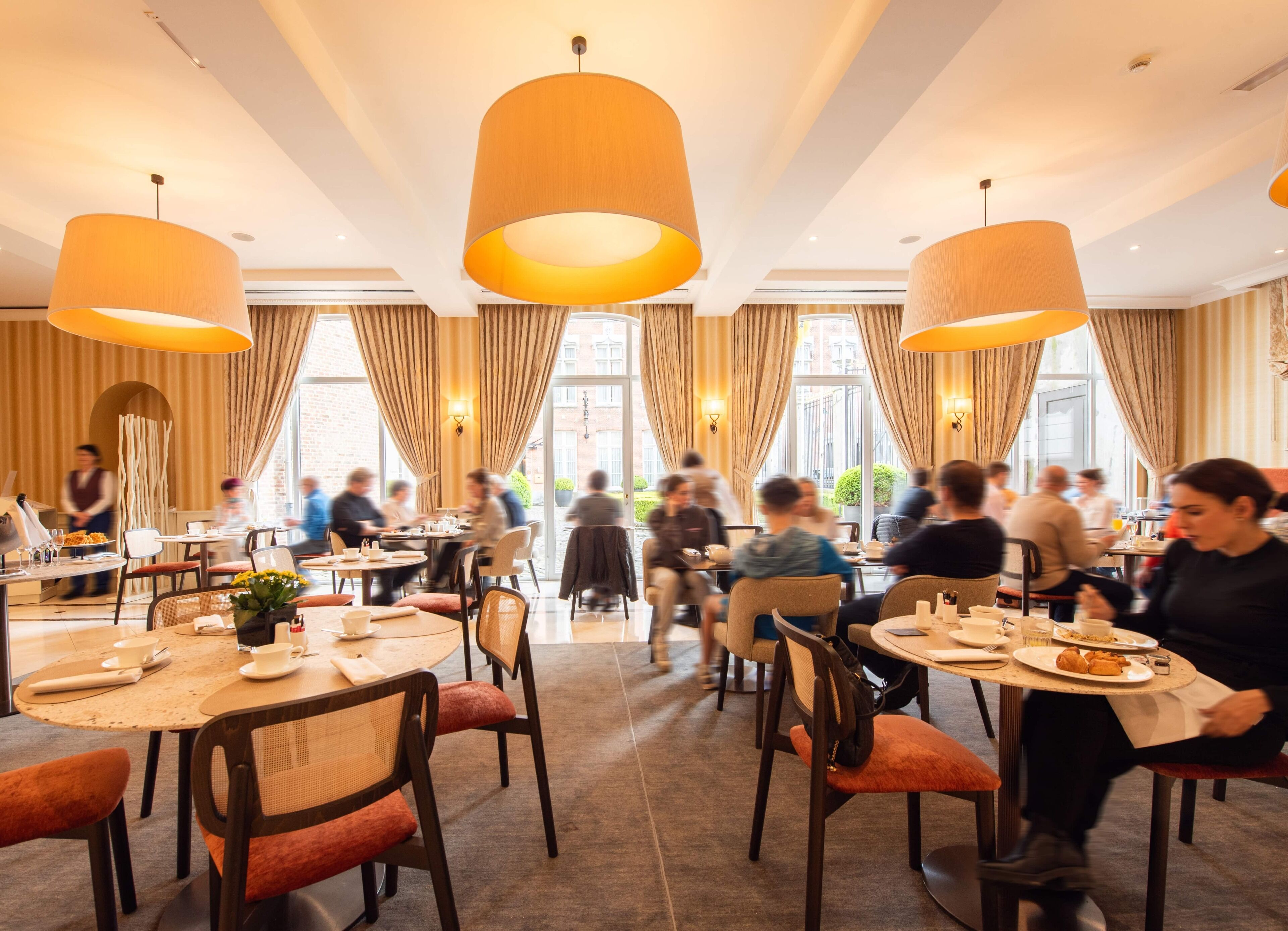 A restaurant with round tables, chairs, and hanging pendant lights.