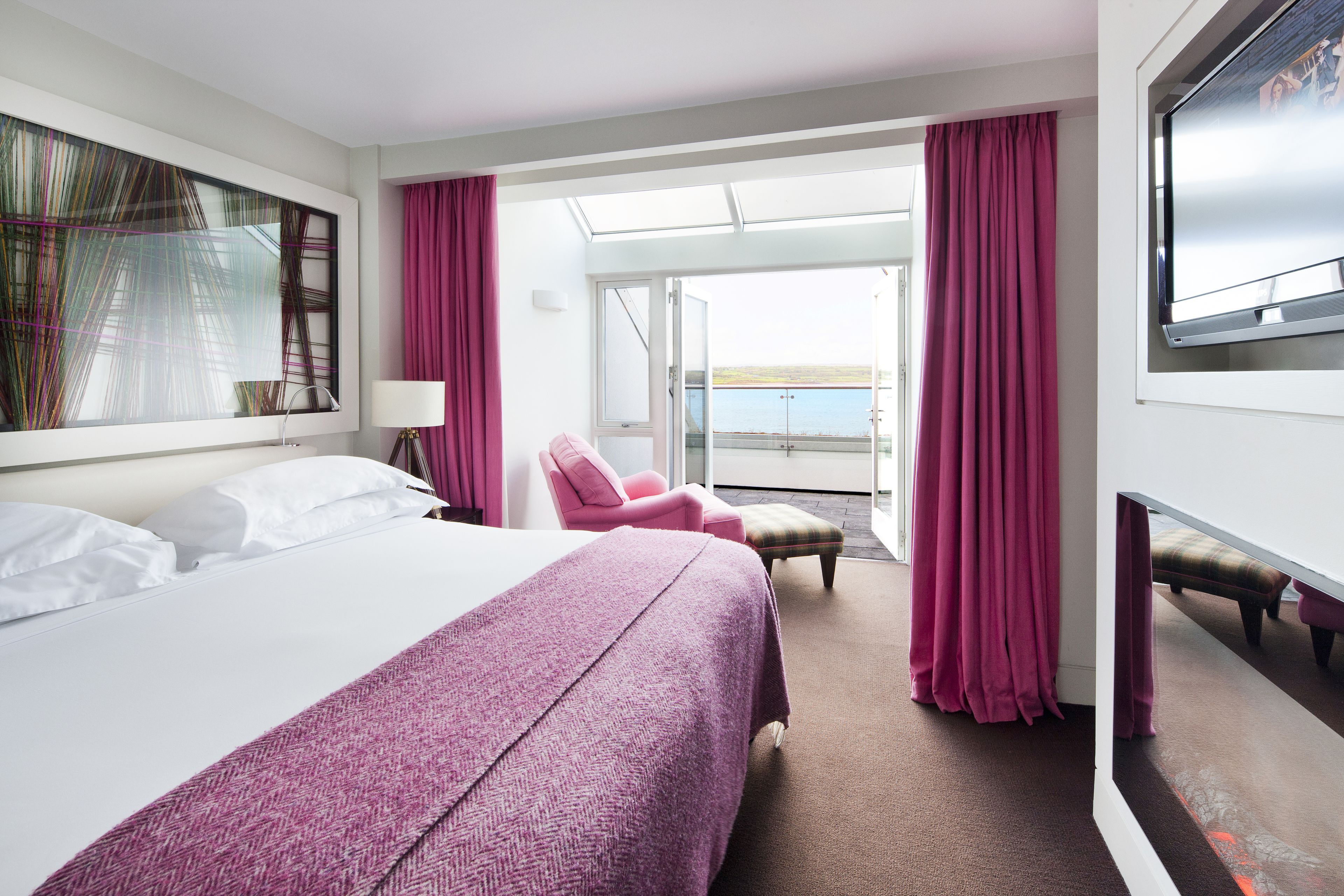 Habitación de hotel con una cama grande, un escritorio, una silla y un televisor. Cuenta con un balcón con vistas al mar.