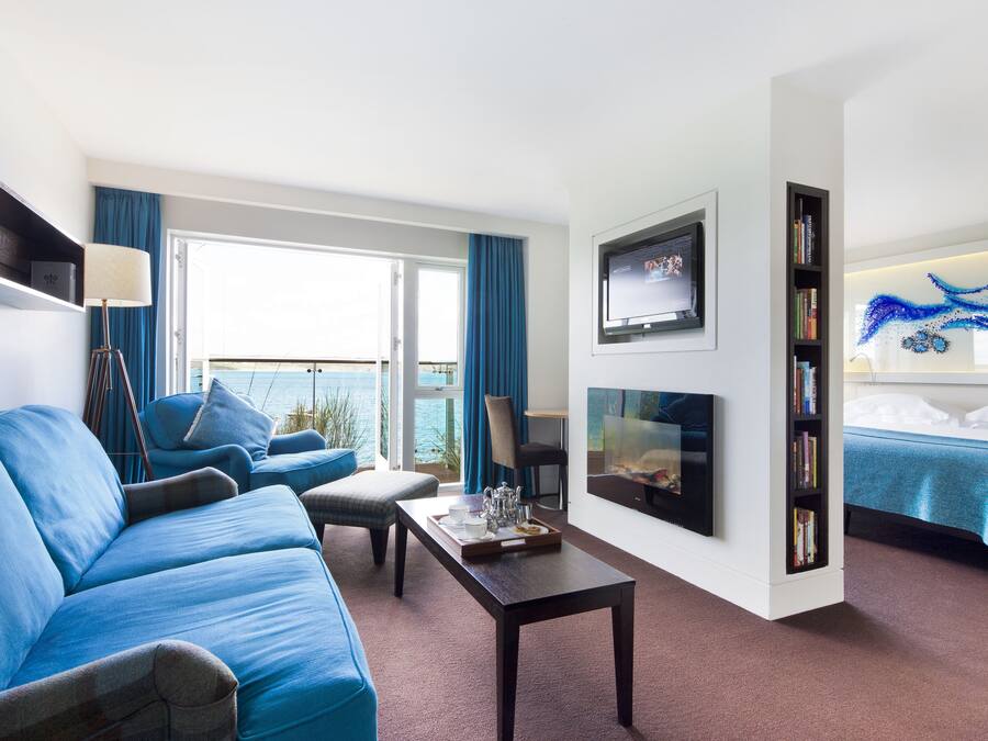 Una habitación de hotel moderna con sofá, una mesa de comedor, televisor, estantería y cama.