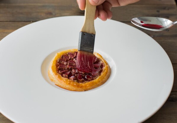 A hand holding a paintbrush over a plate with a pastry. - Cliff House Hotel (Ardmore)
