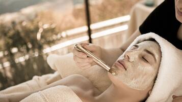 A person receiving a facial treatment in a room with a large window.