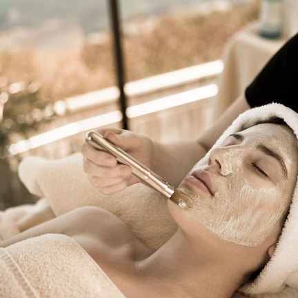 A person receiving a facial treatment in a room with a large window.