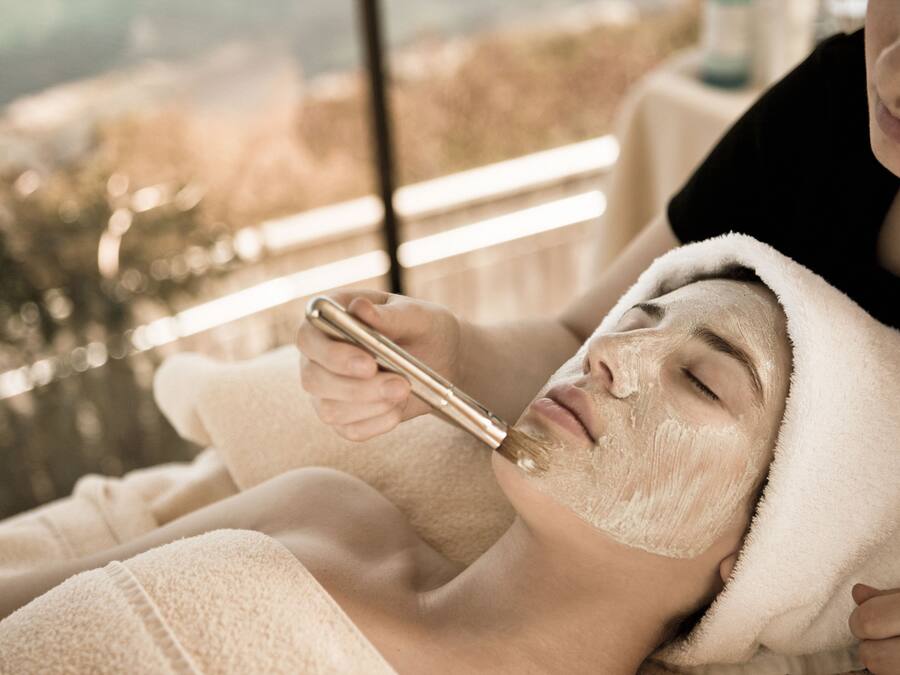 A person receiving a facial treatment in a room with a large window.