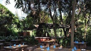 An outdoor dining area with wooden tables and benches, surrounded by lush greenery and trees. - La Mada Hotel (Nairobi)