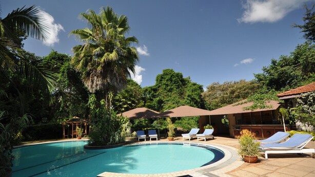 A swimming pool with lounge chairs and umbrellas, surrounded by lush greenery and a gazebo. - La Mada Hotel (Nairobi)