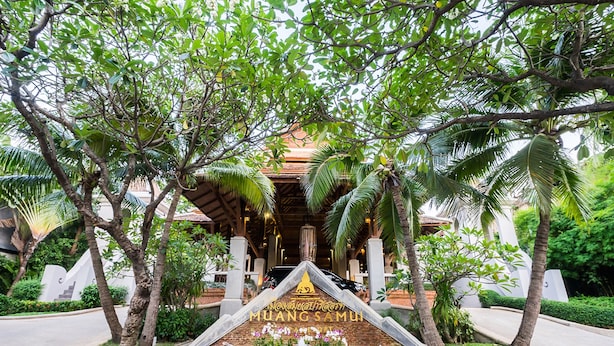 A sign with "MUANGSAMU" and "Orchid" written on it, surrounded by palm trees and a water feature.