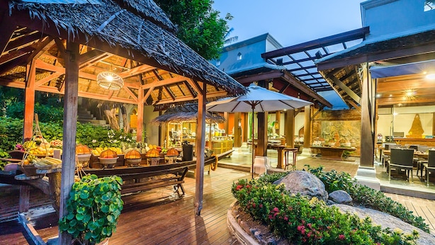 An outdoor dining area with wooden tables and chairs, a thatched-roof structure, and potted plants. - Muang Samui Spa Resort (Koh Samui)