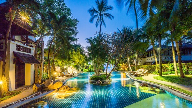 A pool area with lounge chairs and palm trees, surrounded by buildings. - Muang Samui Spa Resort (Koh Samui)