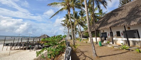 A beachside resort with thatched-roof buildings, palm trees, and a sandy beach.