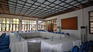 Un salón de conferencias con una larga mesa, sillas azules y manteles blancos.